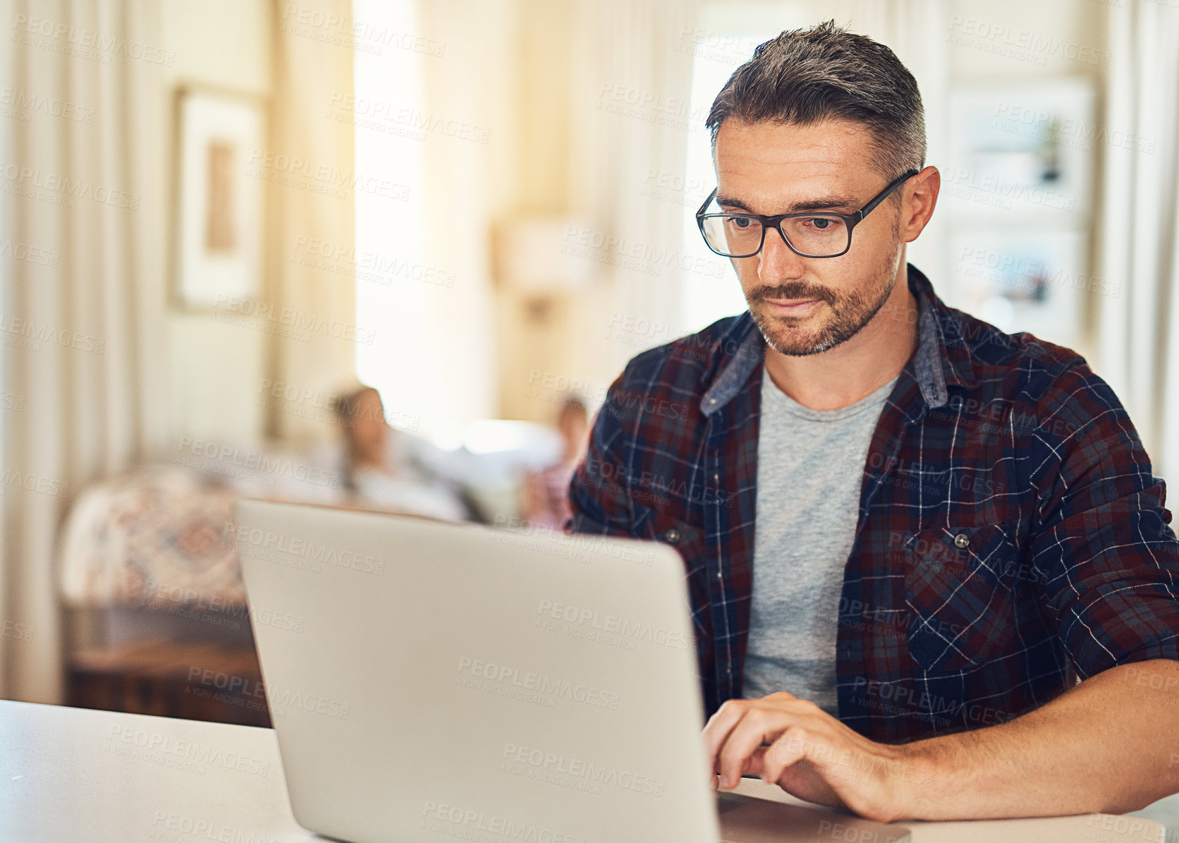 Buy stock photo Cropped shot of a mature man using a laptop at home with his family in the background