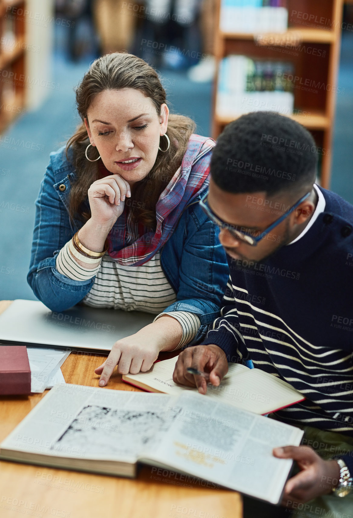 Buy stock photo Shot of two university students working together in the library at campus
