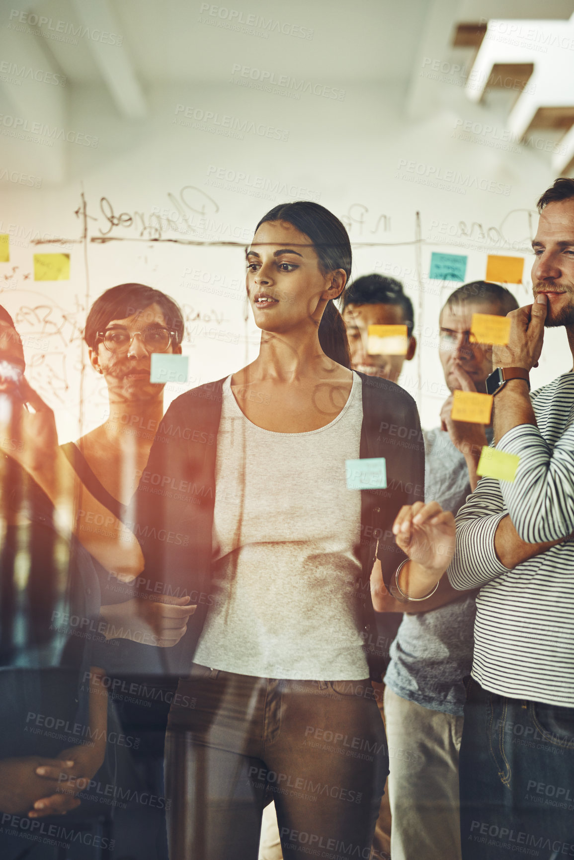 Buy stock photo Group of marketing professionals or designers brainstorming ideas, writing on transparent board with sticky notes during meeting. Diverse team of colleagues discussing work project schedule plan.