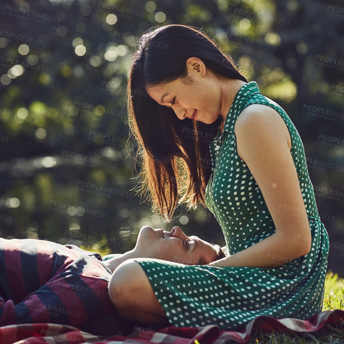 Buy stock photo Shot of an affectionate young couple relaxing together on a picnic blanket in the park