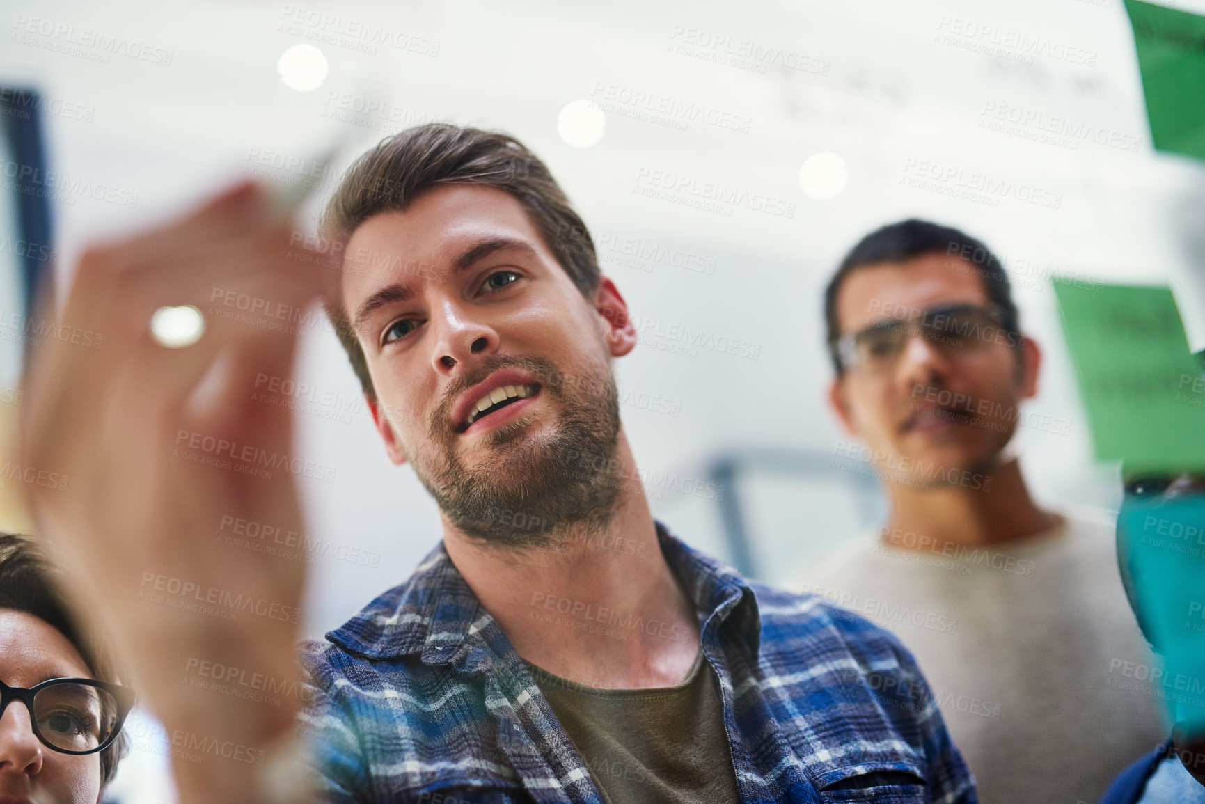 Buy stock photo Shot of a group of designers brainstorming with notes on a glass wall in an office