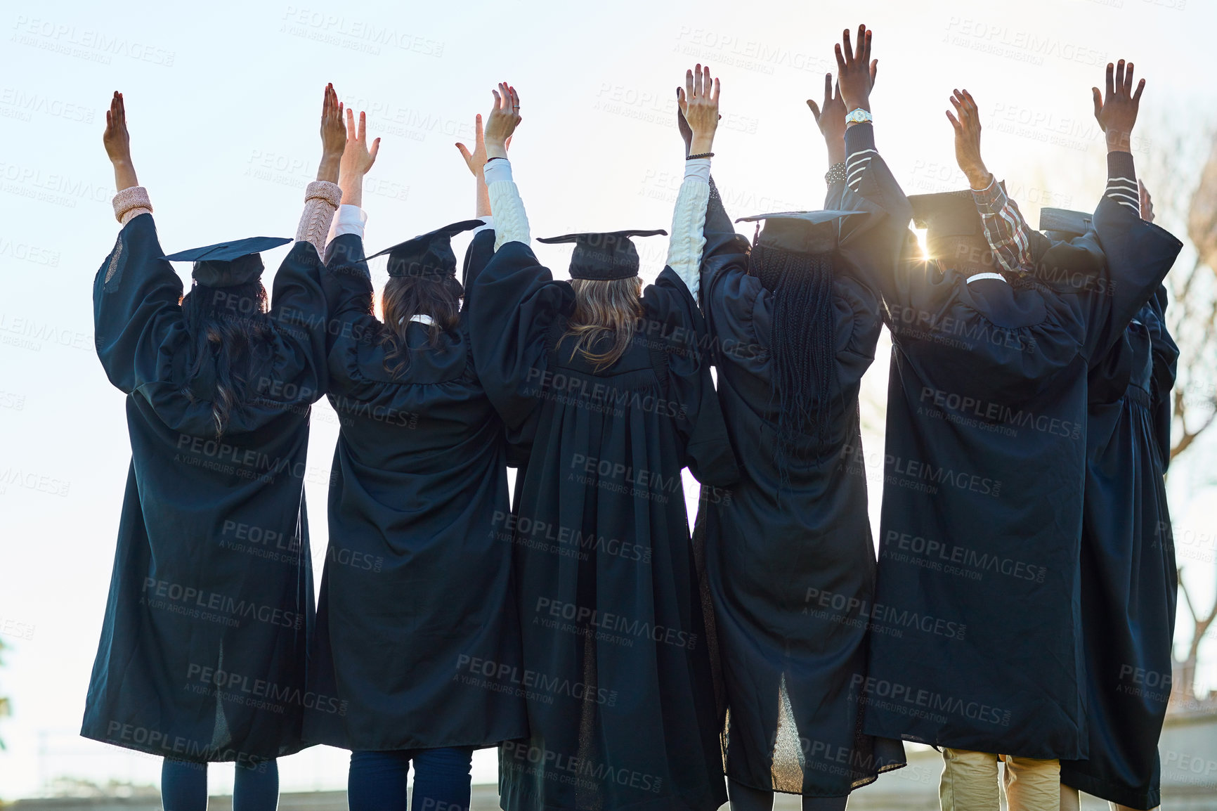 Buy stock photo Rearview shot of a group of students standing in a line with their arms raised on graduation day