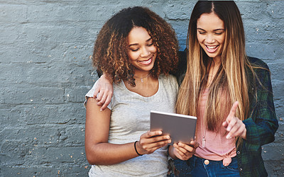 Buy stock photo Shot of two young women standing outdoors and using a digital tablet against a gray wall