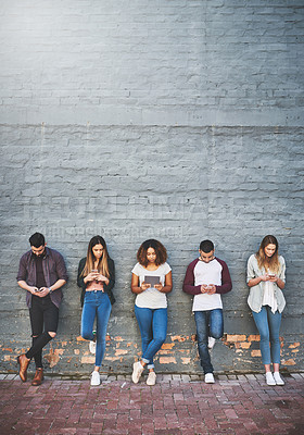 Buy stock photo Shot of a group of young people using their wireless devices together outdoors