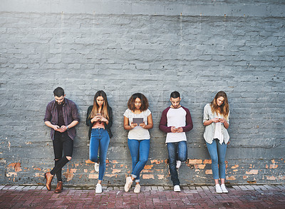 Buy stock photo Shot of a group of young people using their wireless devices together outdoors