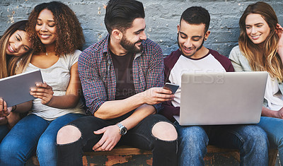 Buy stock photo Shot of a group of young friends using their wireless devices together outdoors