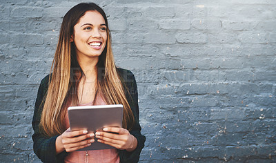 Buy stock photo Shot of a young woman standing outdoors and using a digital tablet against a gray wall