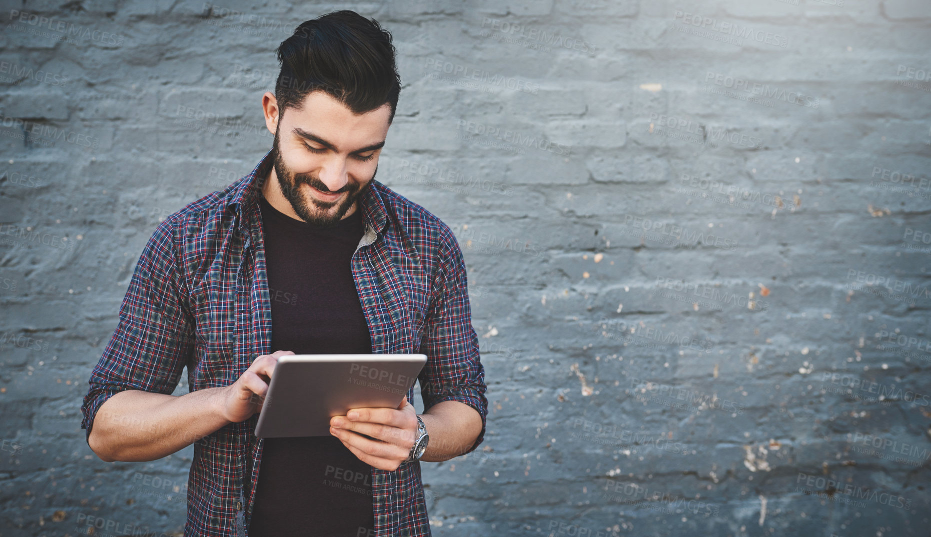 Buy stock photo Shot of a young man standing outdoors and using a digital tablet against a gray wall