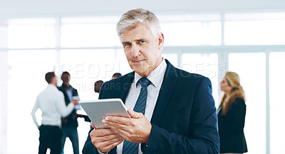 Buy stock photo Cropped portrait of a handsome mature businessman using a tablet in the office with his colleagues in the background