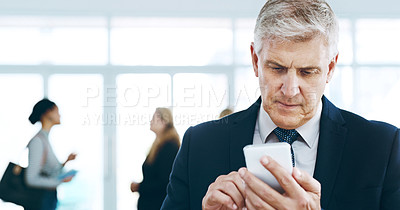 Buy stock photo Cropped shot of a handsome mature businessman using a cellphone in the office with his colleagues in the background