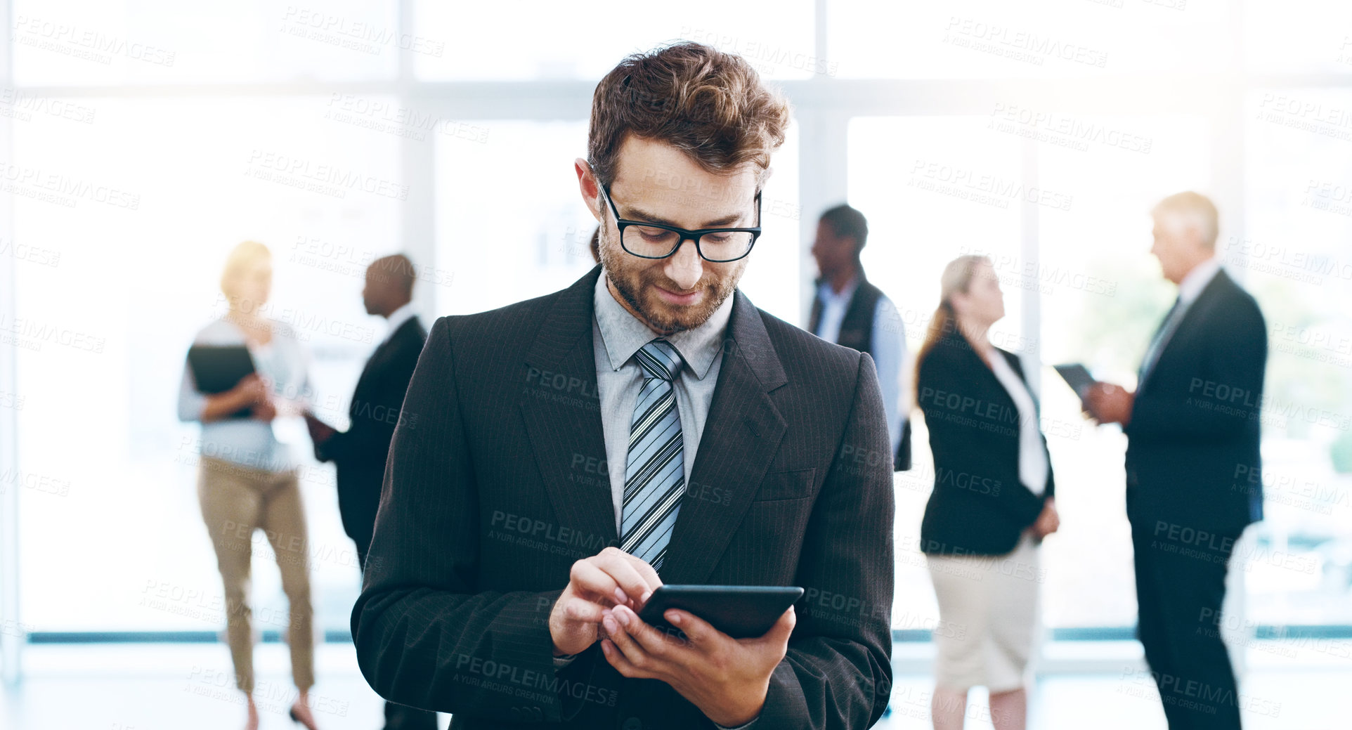 Buy stock photo Cropped shot of a handsome businessman using a tablet in the office with his colleagues in the background
