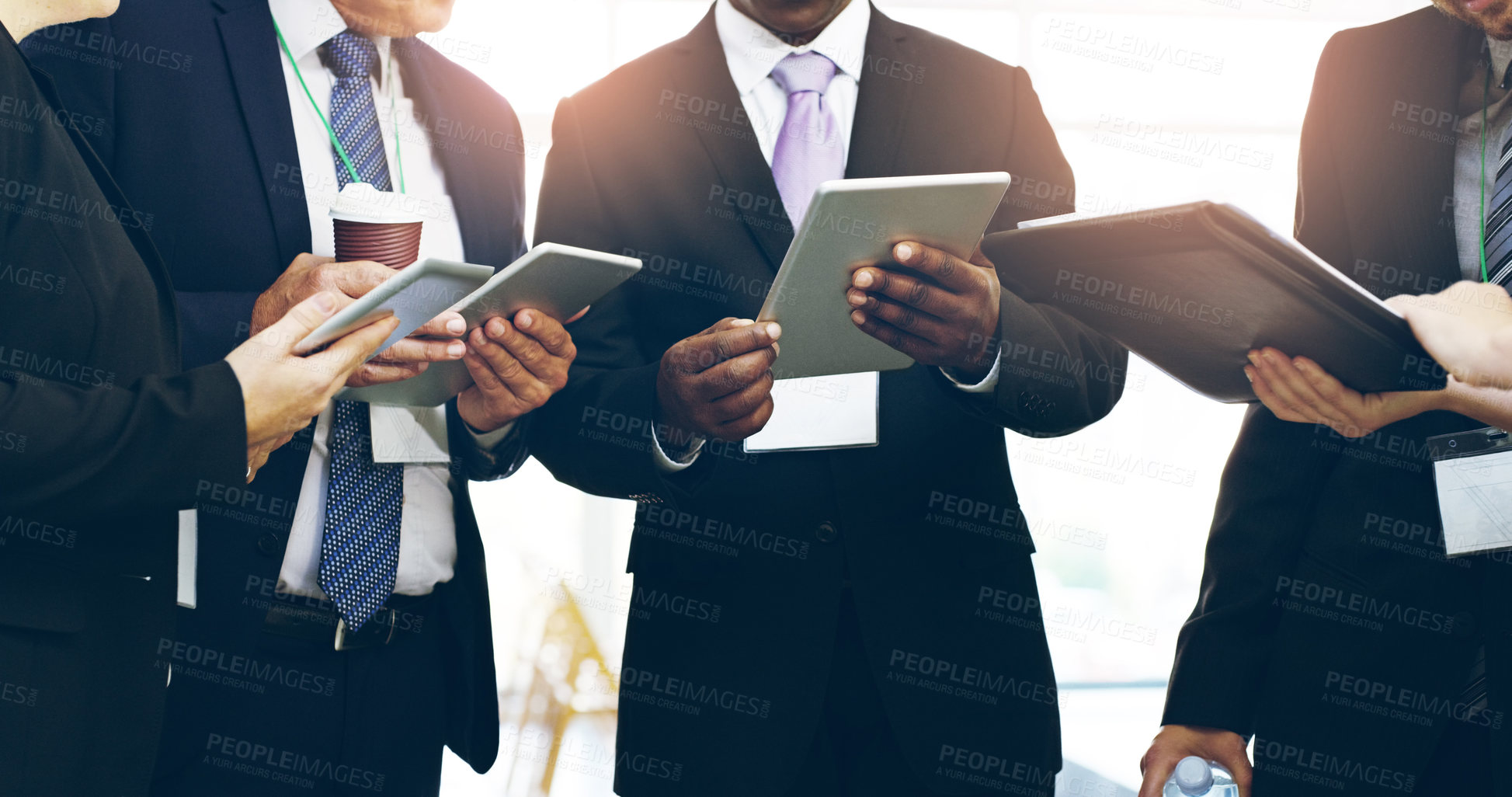 Buy stock photo Cropped shot of a group of unrecognizable businesspeople standing in a huddle with digital tablets in hand