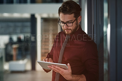 Buy stock photo Shot of a young businessman using a digital tablet in a modern office