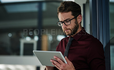 Buy stock photo Shot of a young businessman using a digital tablet in a modern office