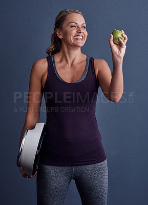 Buy stock photo Studio shot of an attractive mature woman holding an apple and a weightscale against a blue background