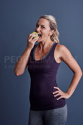 Buy stock photo Studio portrait of an attractive mature woman biting into an apple against a blue background