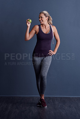Buy stock photo Studio shot of an attractive mature woman holding an apple against a blue background