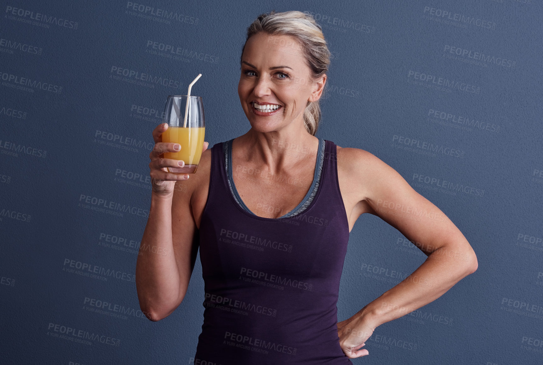 Buy stock photo Studio portrait of an attractive mature woman in sportswear drinking orange juice against a blue background