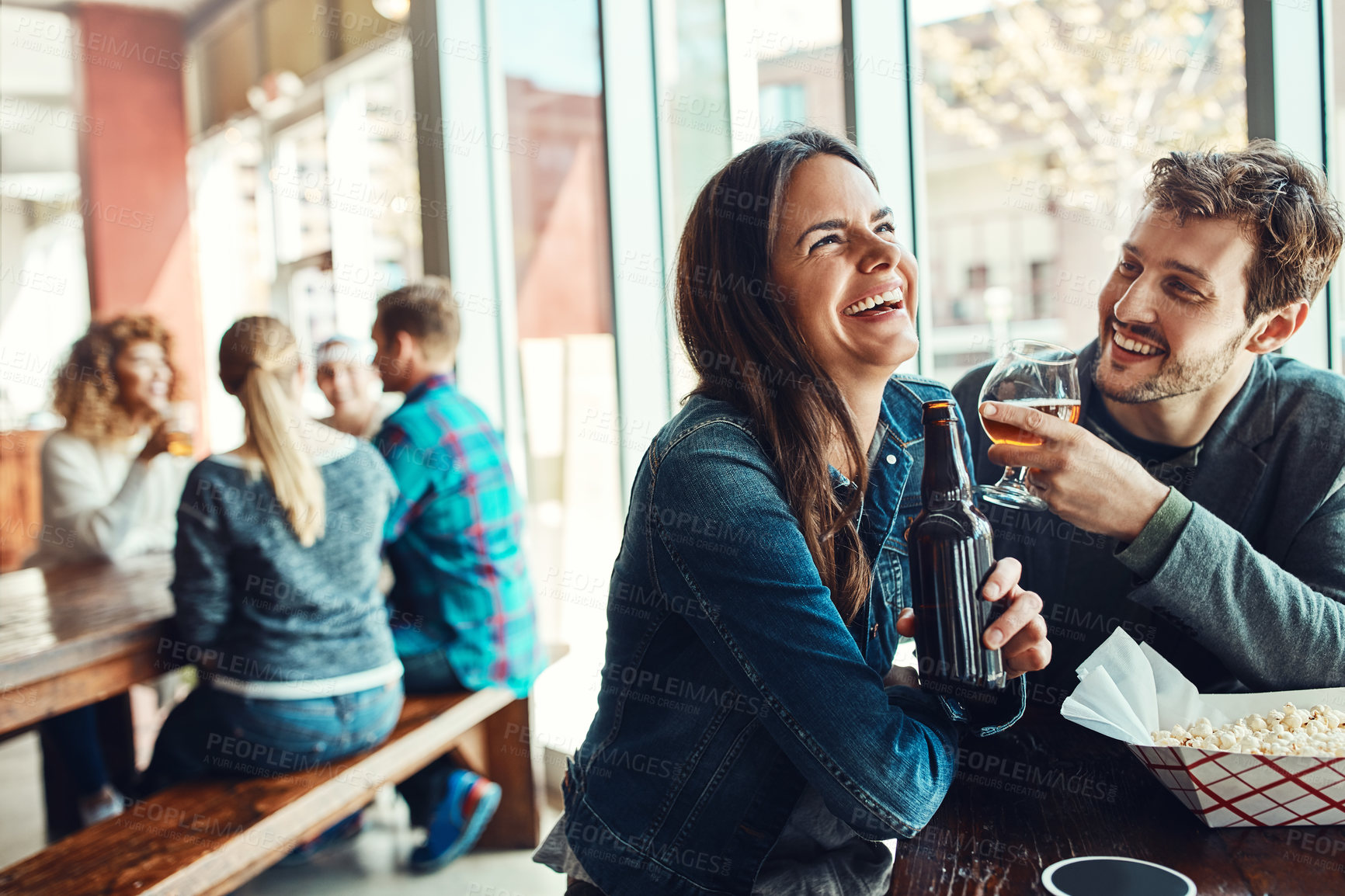 Buy stock photo Cropped shot of a young couple having drinks in a bar with people blurred in the background