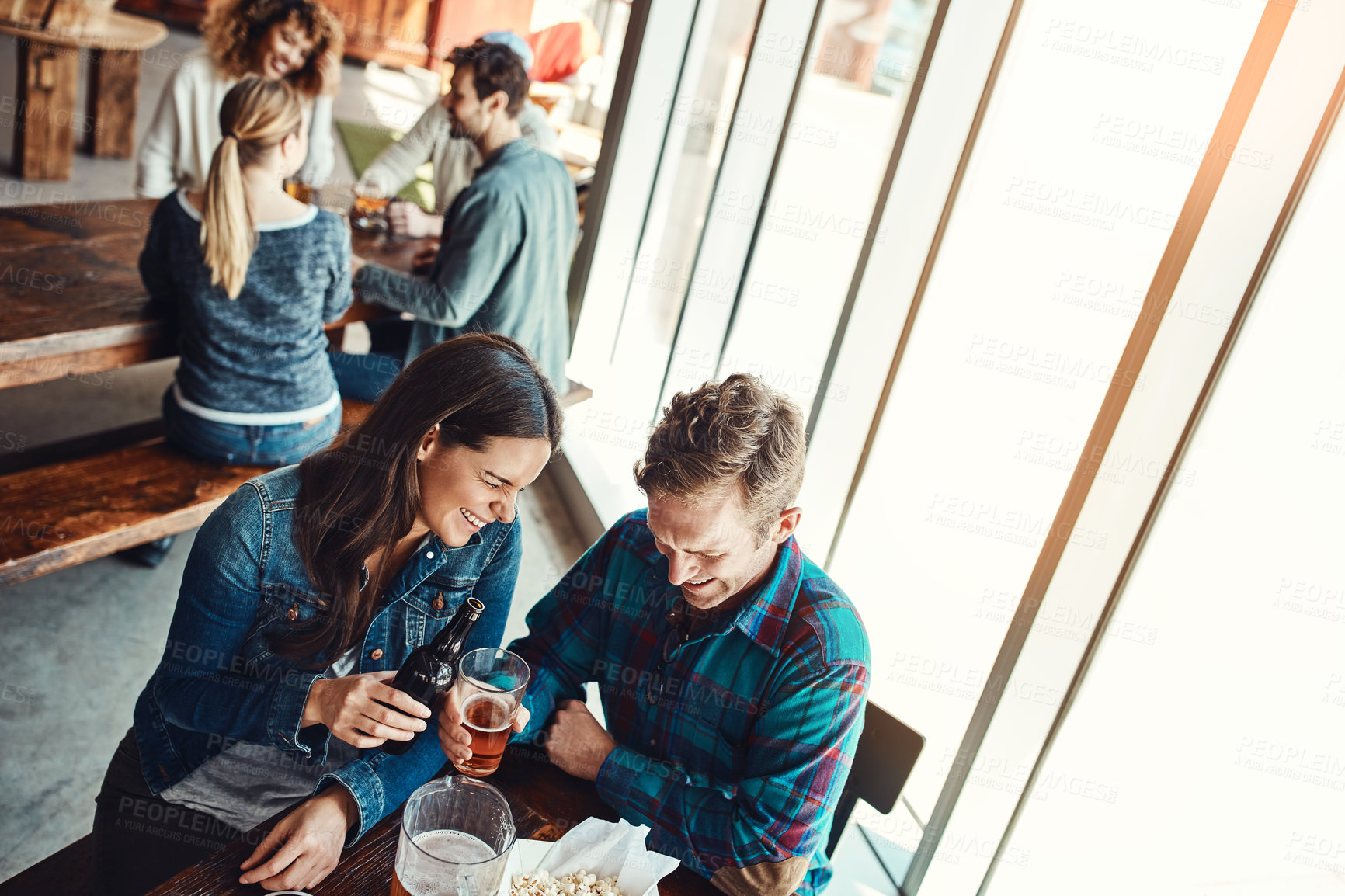 Buy stock photo Cropped shot of a young couple having drinks in a bar with people blurred in the background