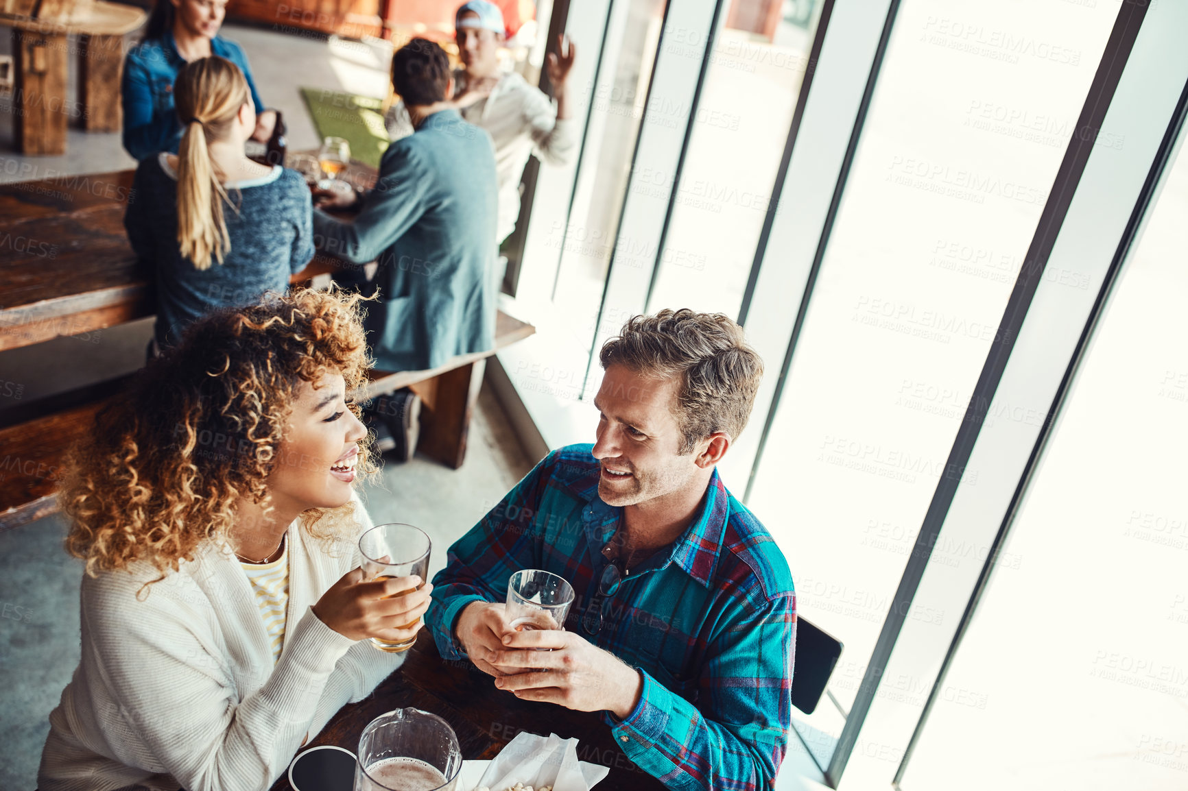 Buy stock photo Cropped shot of a young couple having drinks in a bar with people blurred in the background