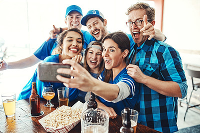 Buy stock photo Shot of a group of friends taking a selfie while watching a sports game at a bar