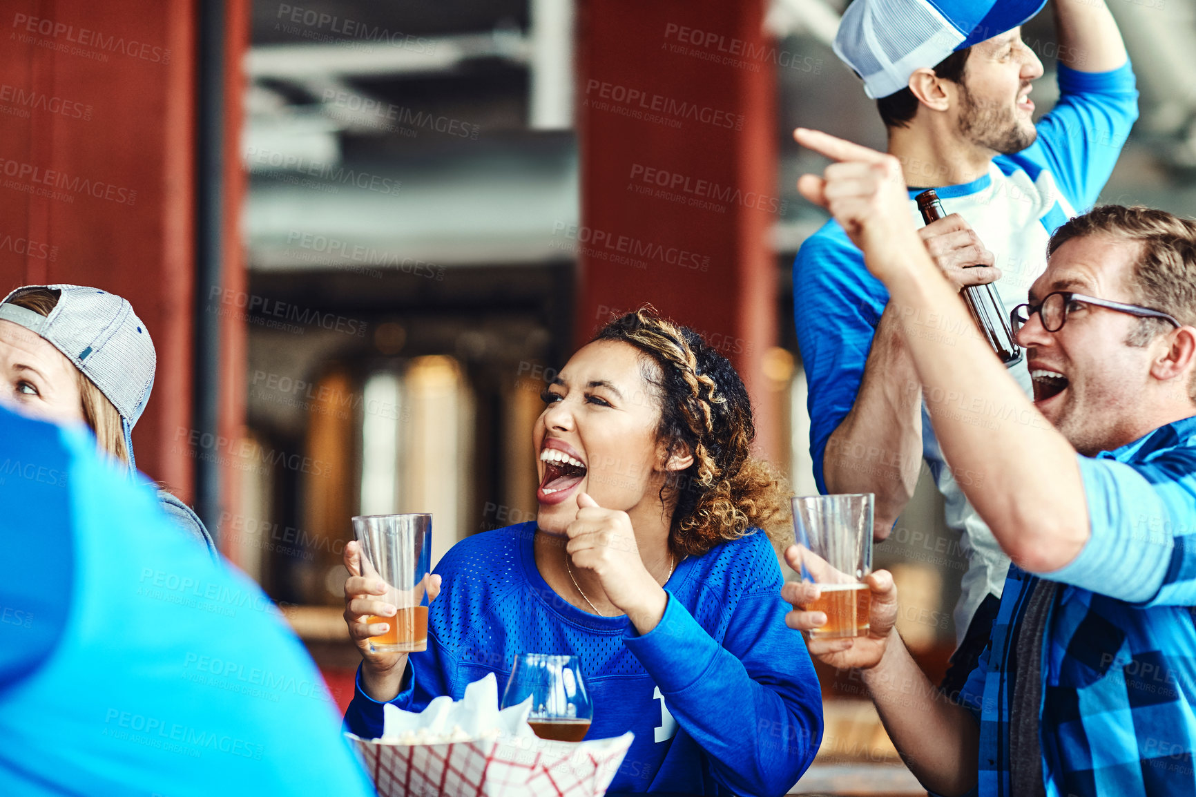 Buy stock photo Shot of a group of friends cheering while watching a sports game at a bar