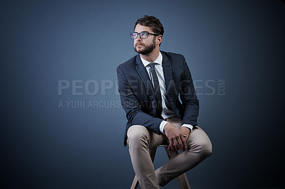 Buy stock photo Studio shot of a handsome young businessman looking thoughtful while sitting on a chair against a dark background