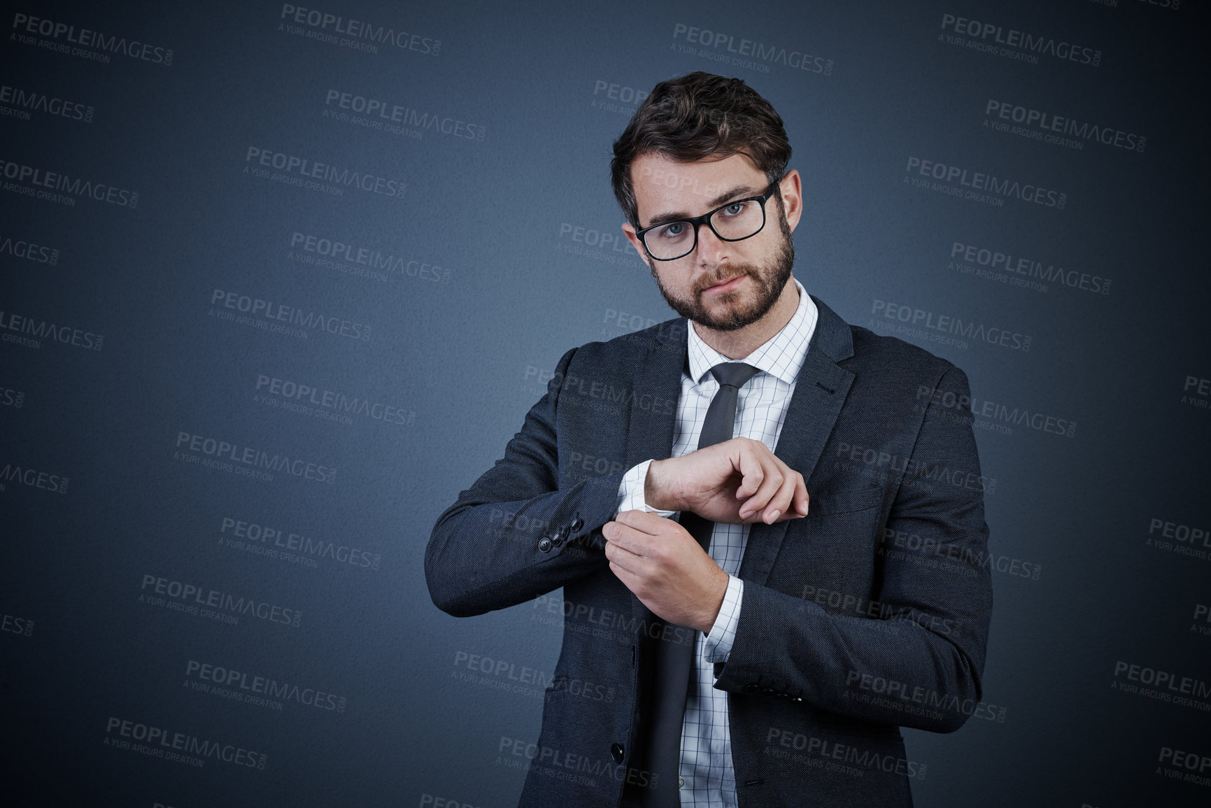 Buy stock photo Studio portrait of a handsome young businessman adjusting his cuffs against a dark background