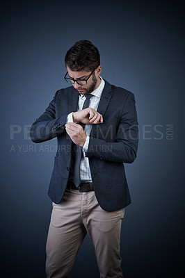 Buy stock photo Studio shot of a handsome young businessman adjusting his cuffs against a dark background