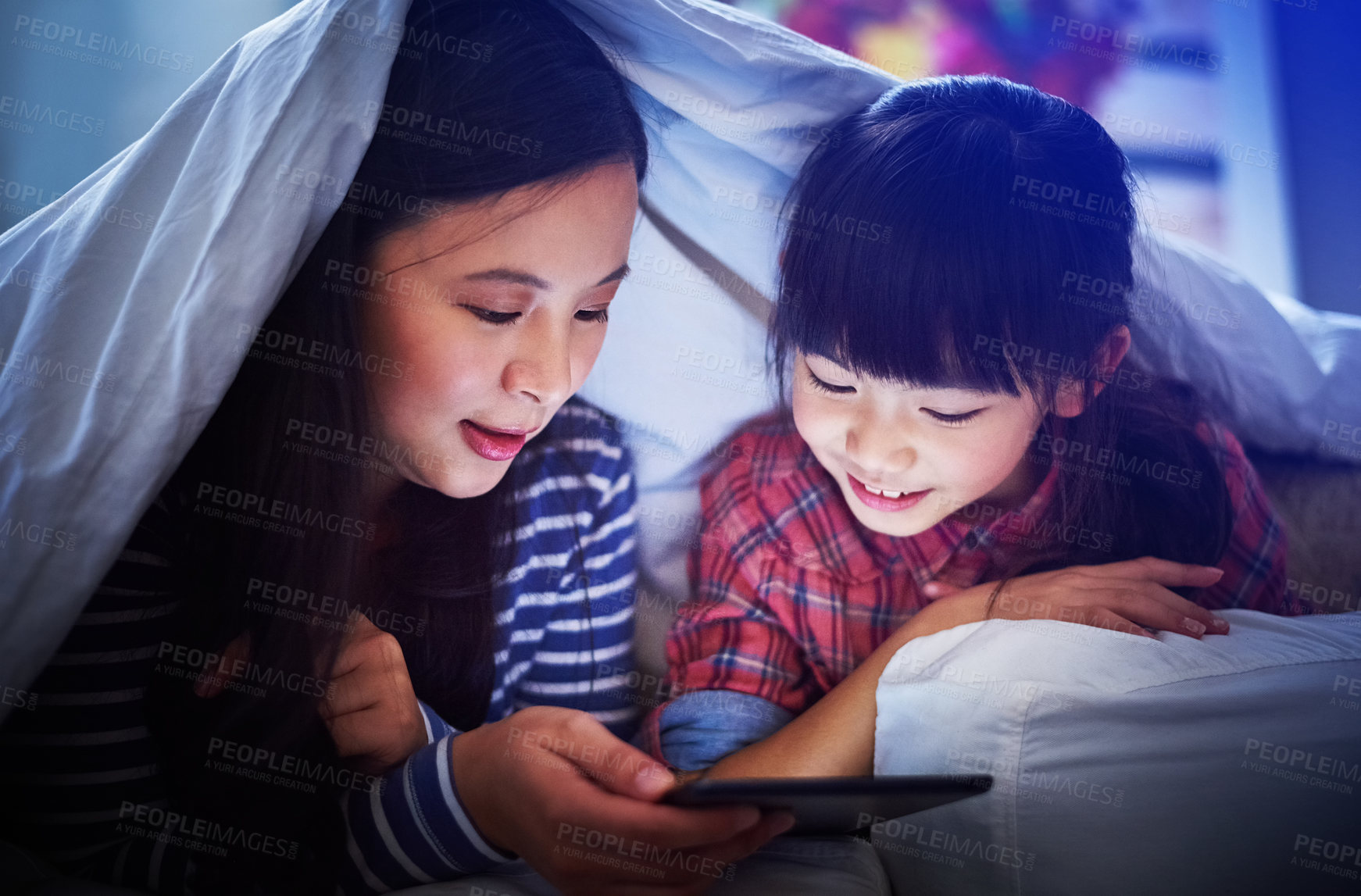 Buy stock photo Cropped shot of an attractive young woman and her daughter using a digital tablet while lying under the covers