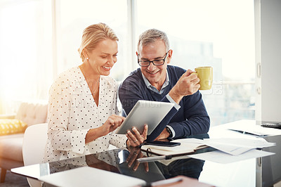 Buy stock photo Shot of a mature couple using a digital tablet while going through paperwork at home