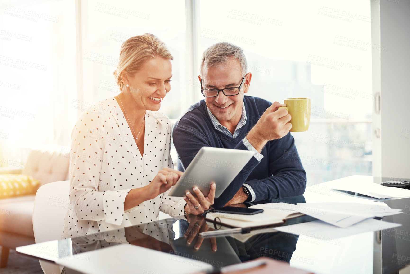 Buy stock photo Shot of a mature couple using a digital tablet while going through paperwork at home