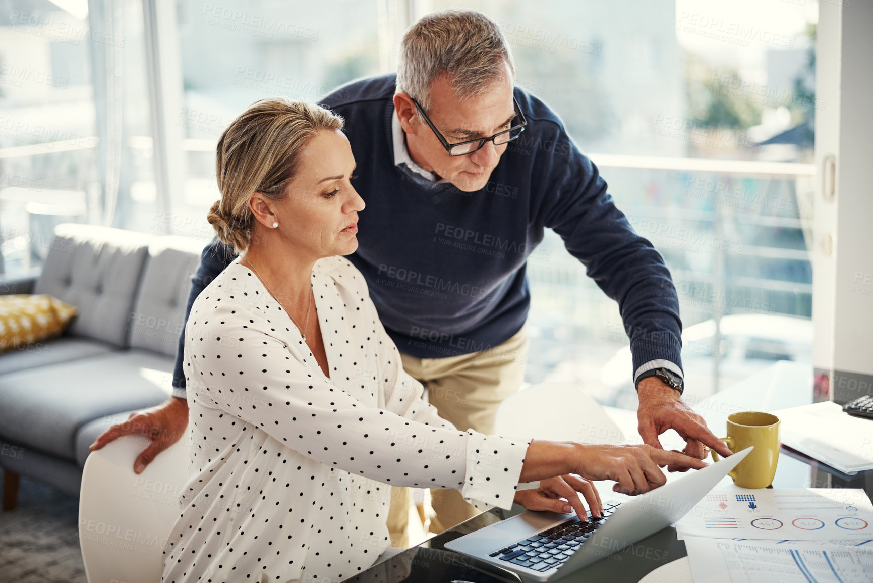 Buy stock photo Shot of a mature couple using a laptop while going through paperwork at home