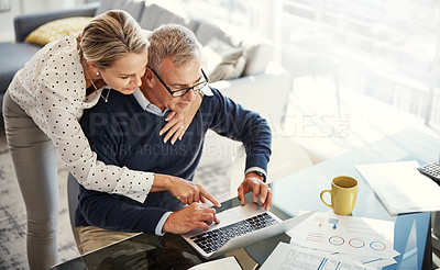 Buy stock photo Shot of a mature couple using a laptop while going through paperwork at home
