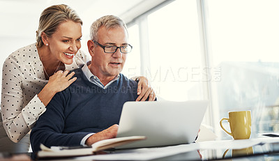 Buy stock photo Shot of a mature couple using a laptop while going through paperwork at home