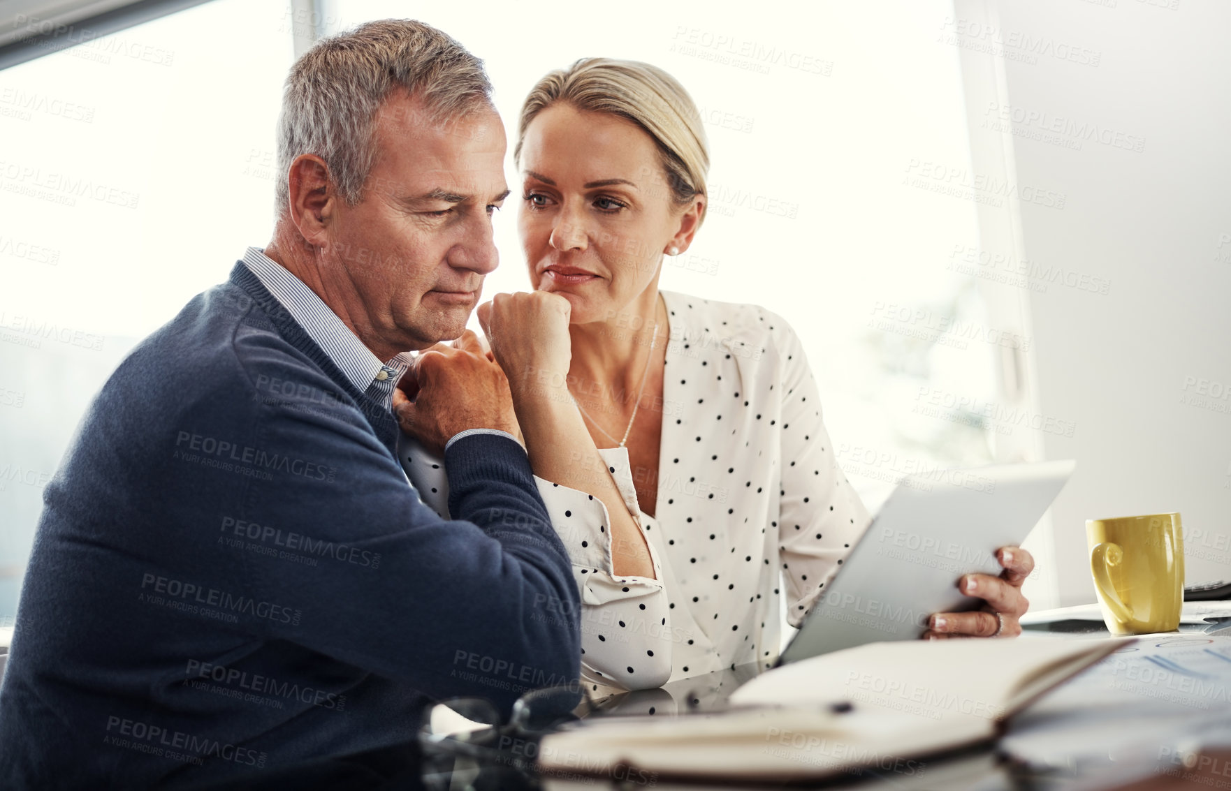 Buy stock photo Shot of a mature couple using a digital tablet while going through paperwork at home