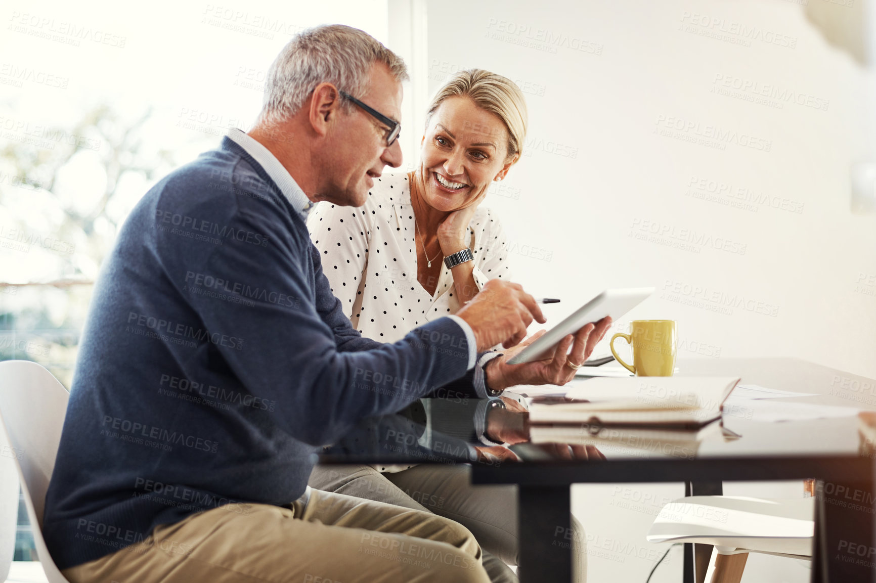 Buy stock photo Shot of a mature couple using a digital tablet while going through paperwork at home