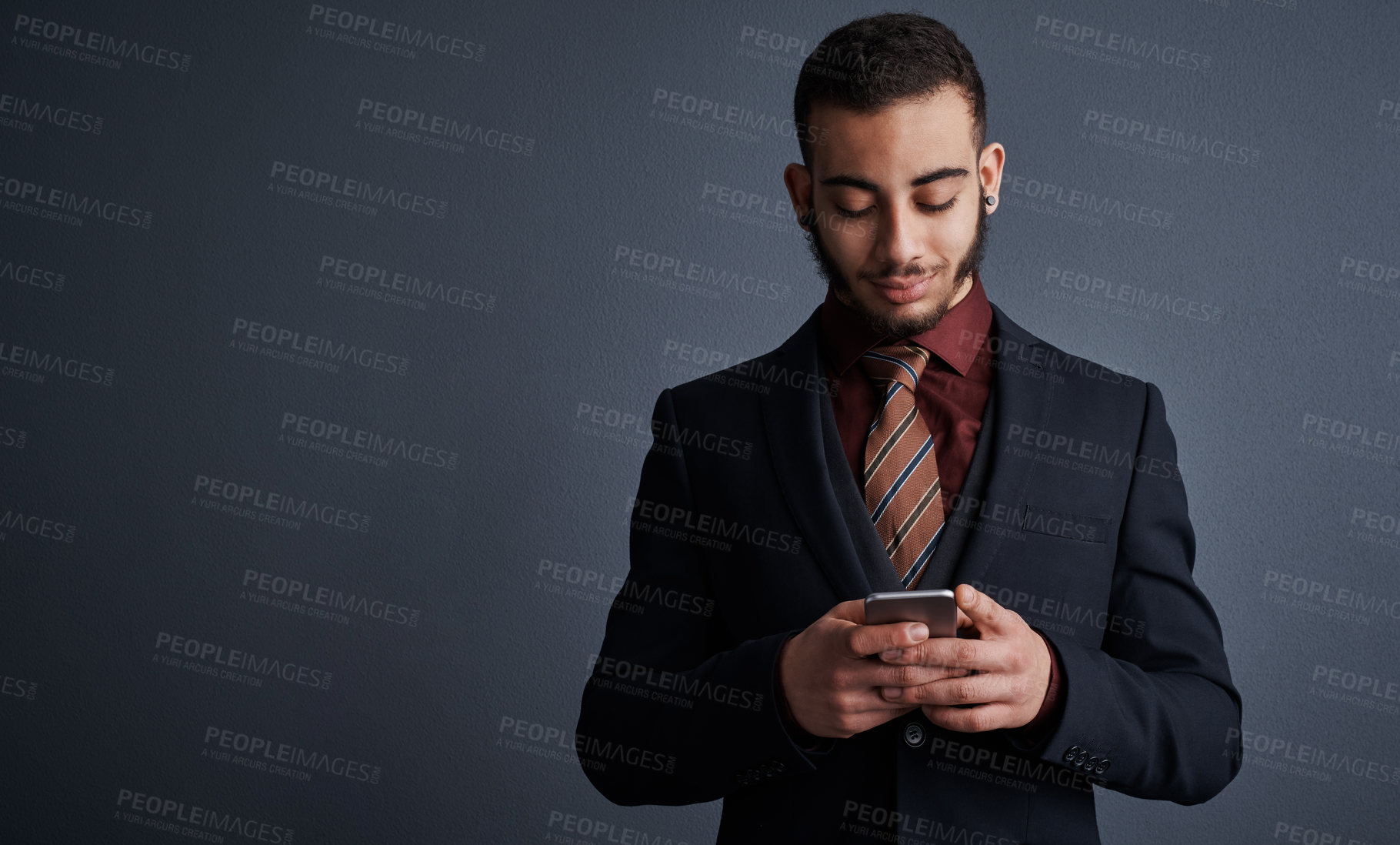 Buy stock photo Studio shot of a stylish young businessman sending a text message while standing against a gray background