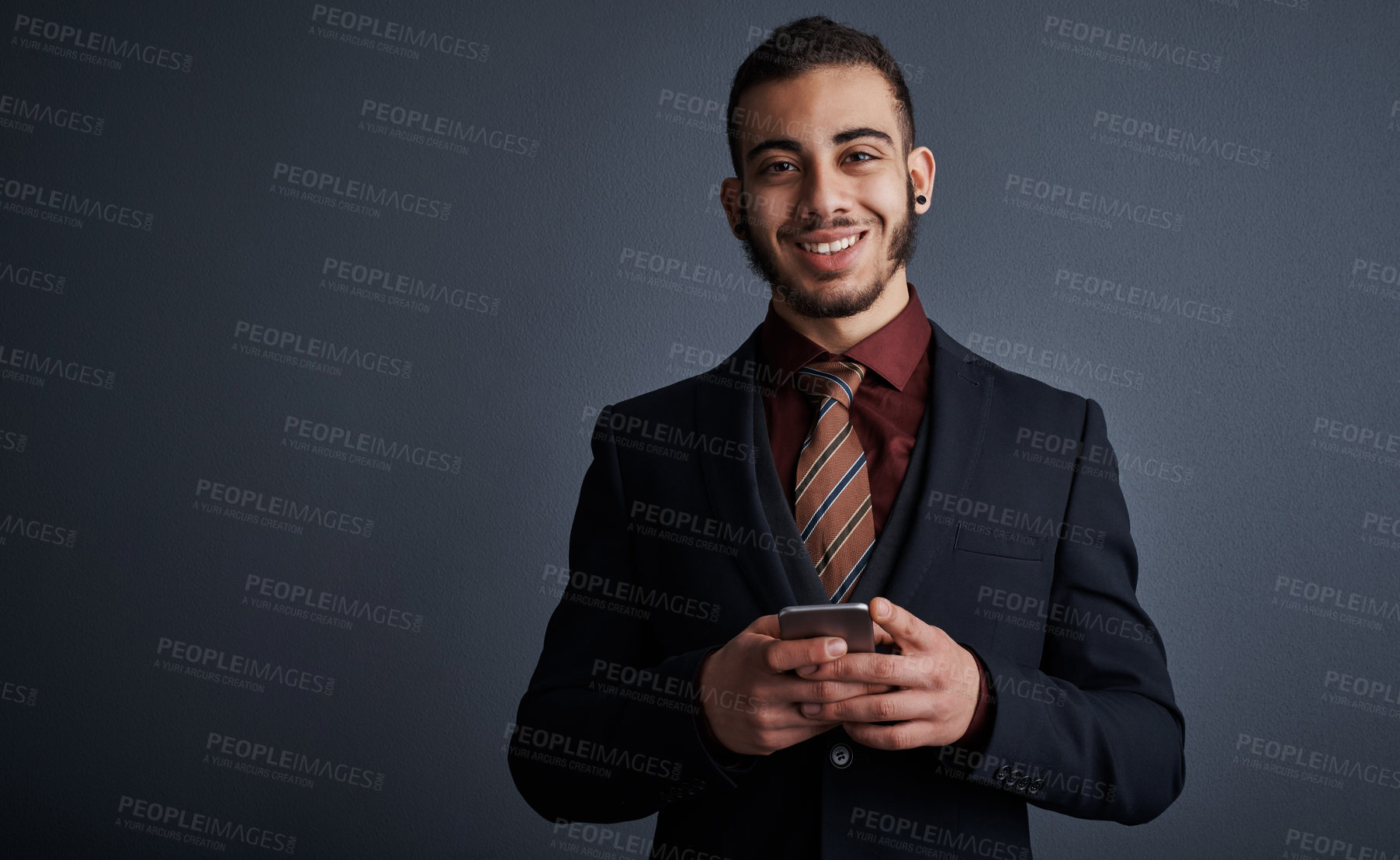 Buy stock photo Studio portrait of a stylish young businessman sending a text message while standing against a gray background