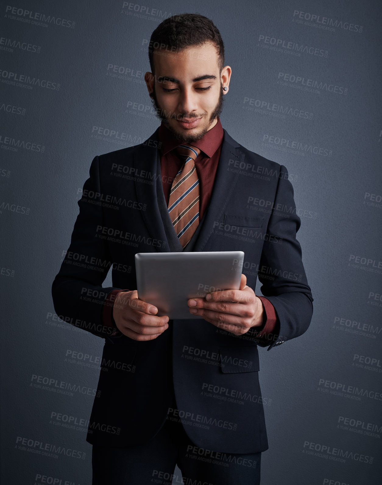 Buy stock photo Studio shot of a stylish young businessman using a tablet against a gray background