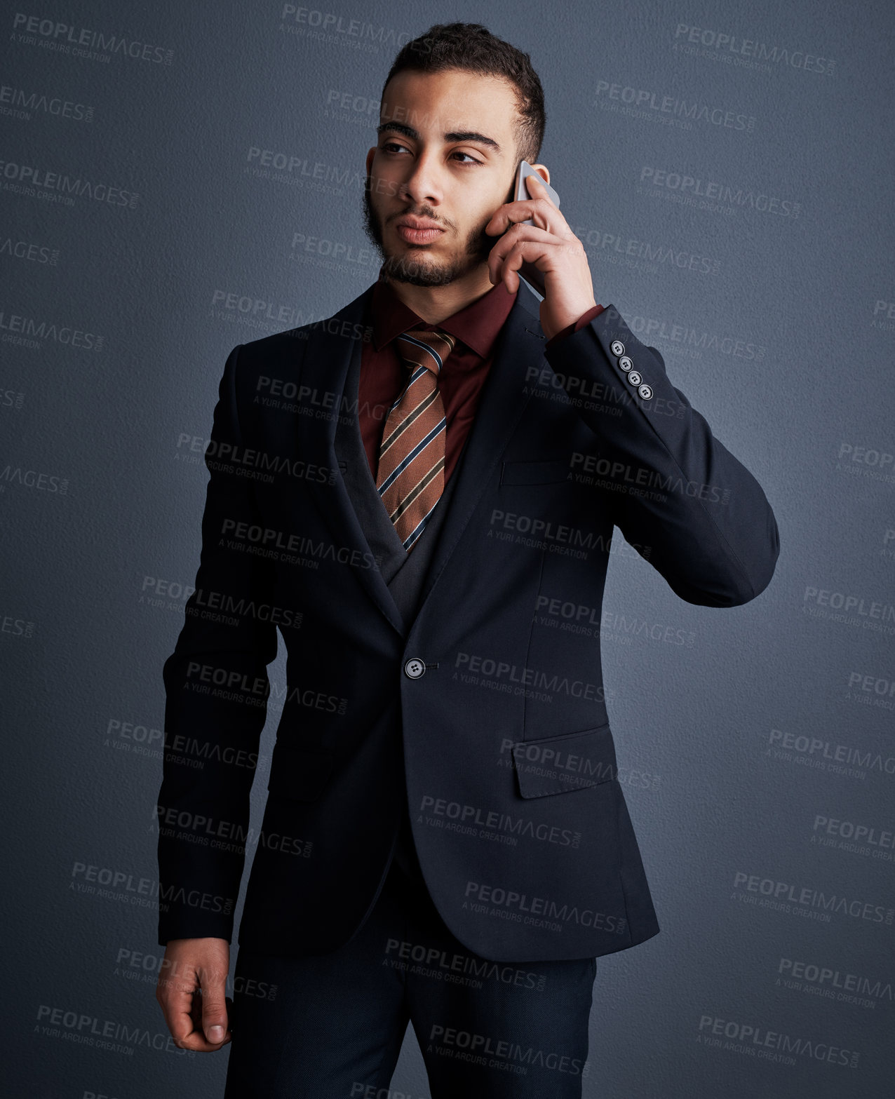 Buy stock photo Studio shot of a stylish young businessman looking thoughtful while making a phonecall against a gray background