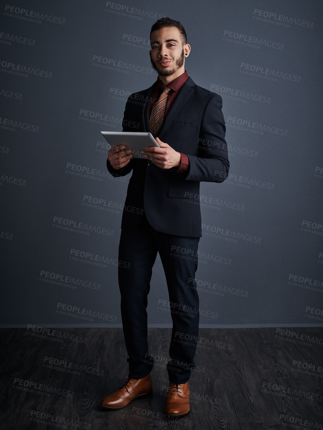 Buy stock photo Studio portrait of a stylish young businessman using a tablet against a gray background