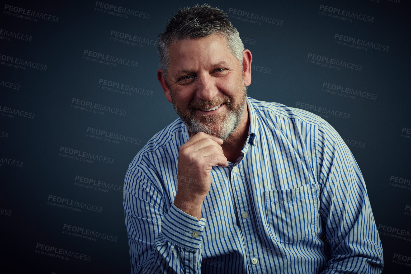 Buy stock photo Studio portrait of a confident and mature businessman sitting with his hand on his chin against a dark background