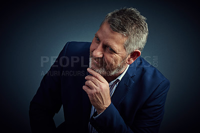 Buy stock photo Studio shot of a confident and mature businessman sitting with his hand on his chin against a dark background