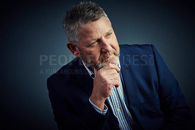 Buy stock photo Studio shot of a confident and mature businessman sitting with his hand on his chin against a dark background
