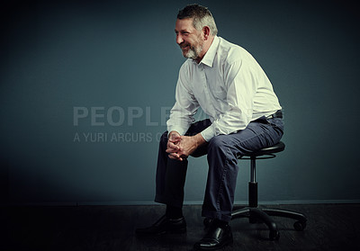 Buy stock photo Studio shot of a handsome mature businessman looking thoughtful while sitting down against a dark background