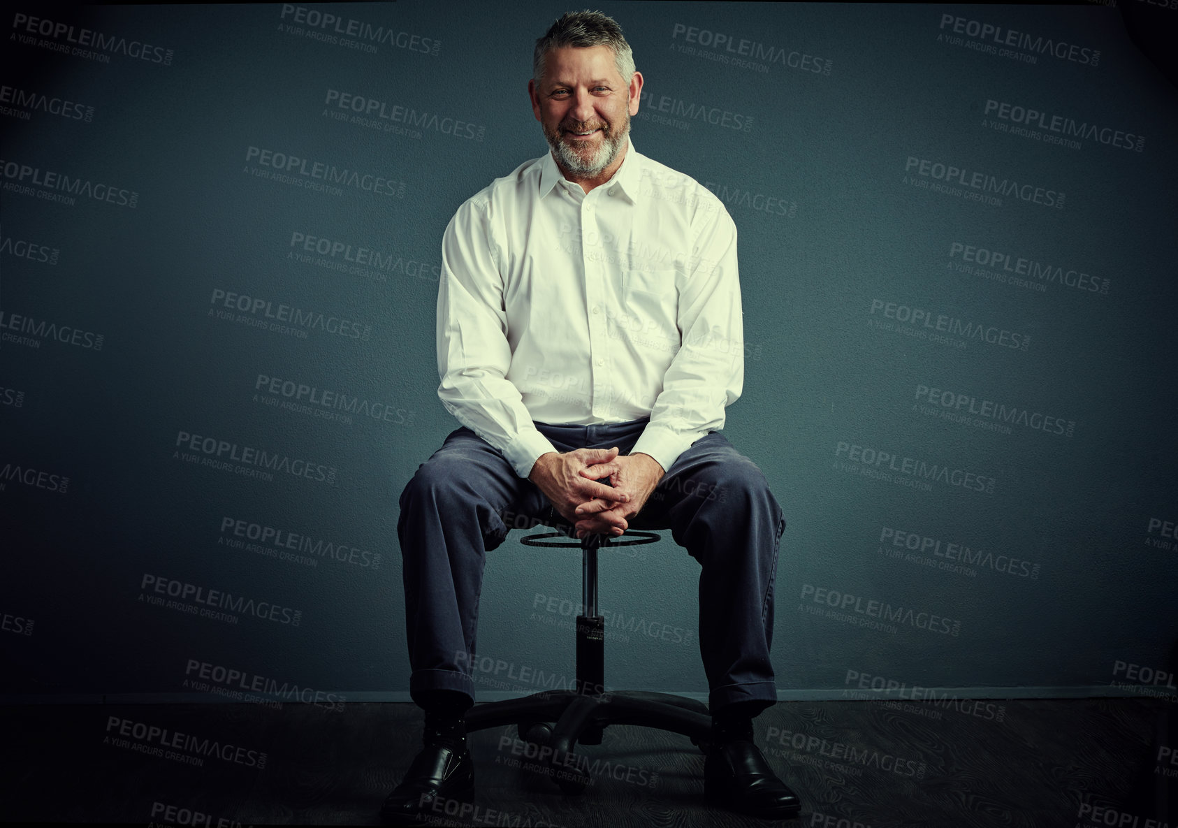 Buy stock photo Studio portrait of a handsome mature businessman sitting down against a dark background