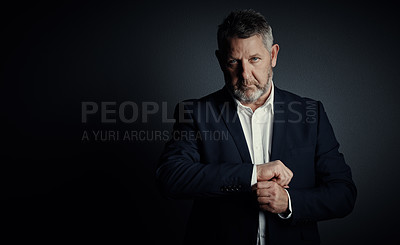 Buy stock photo Studio portrait of a handsome mature businessman buttoning his sleeves while standing against a dark background