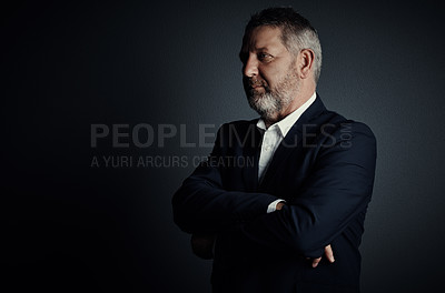 Buy stock photo Studio shot of a handsome mature businessman looking thoughtful while standing with his arms folded against a dark background